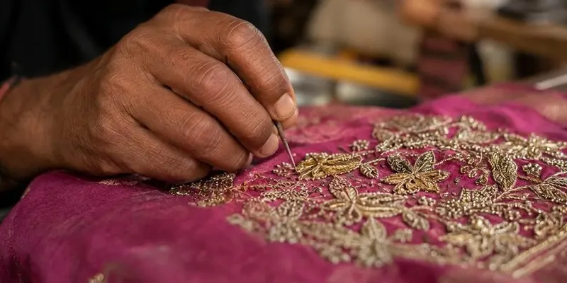 Close-up of hands hand-embroidering gold thread detail onto pink fabric